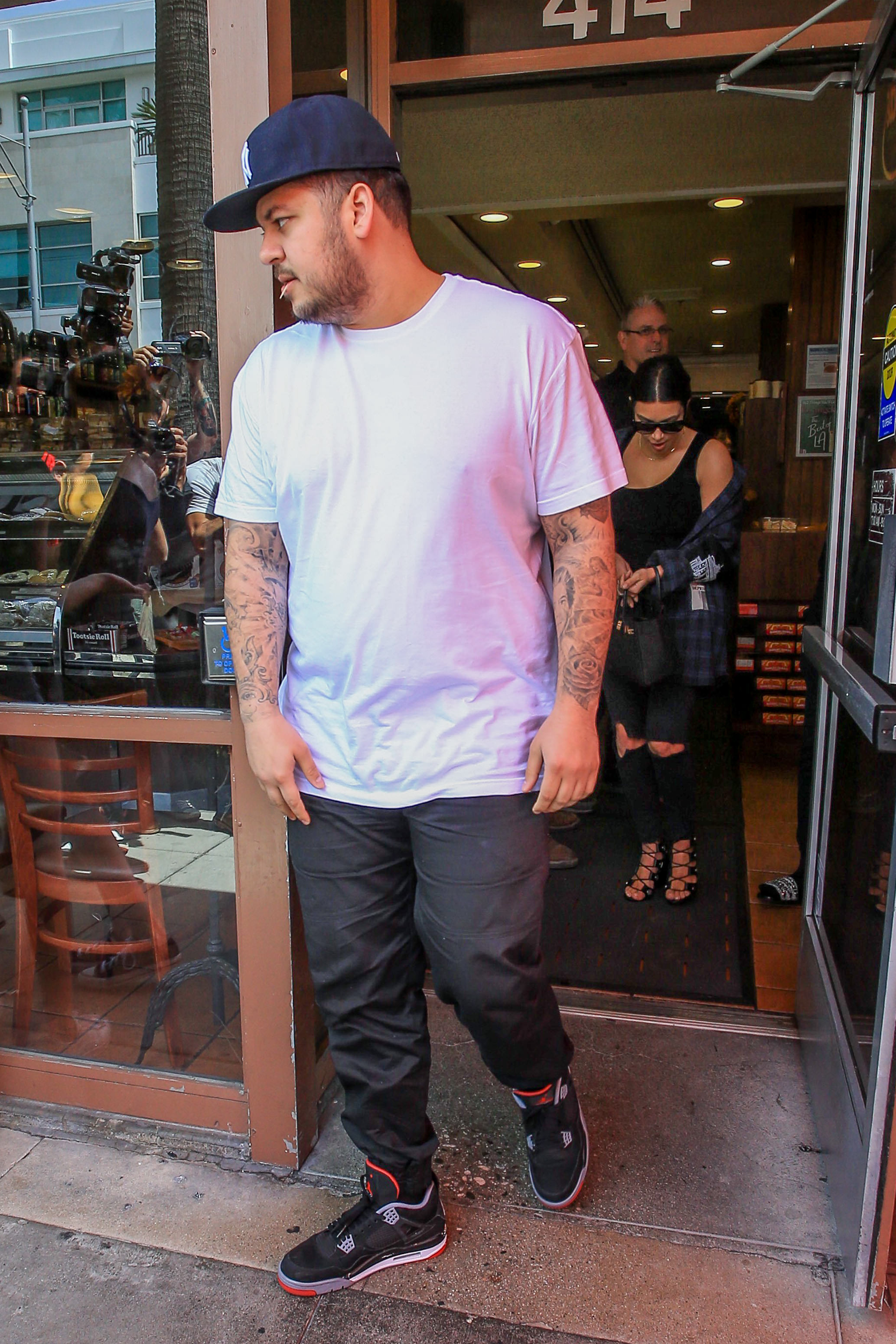 Rob Kardashian steps out of a Los Angeles restaurant in a white T-shirt and baseball cap, with Kim Kardashian following behind him. The photograph captures a rare public outing with his sister during a period when he was gradually becoming more comfortable appearing in public. | Source: Getty Images.