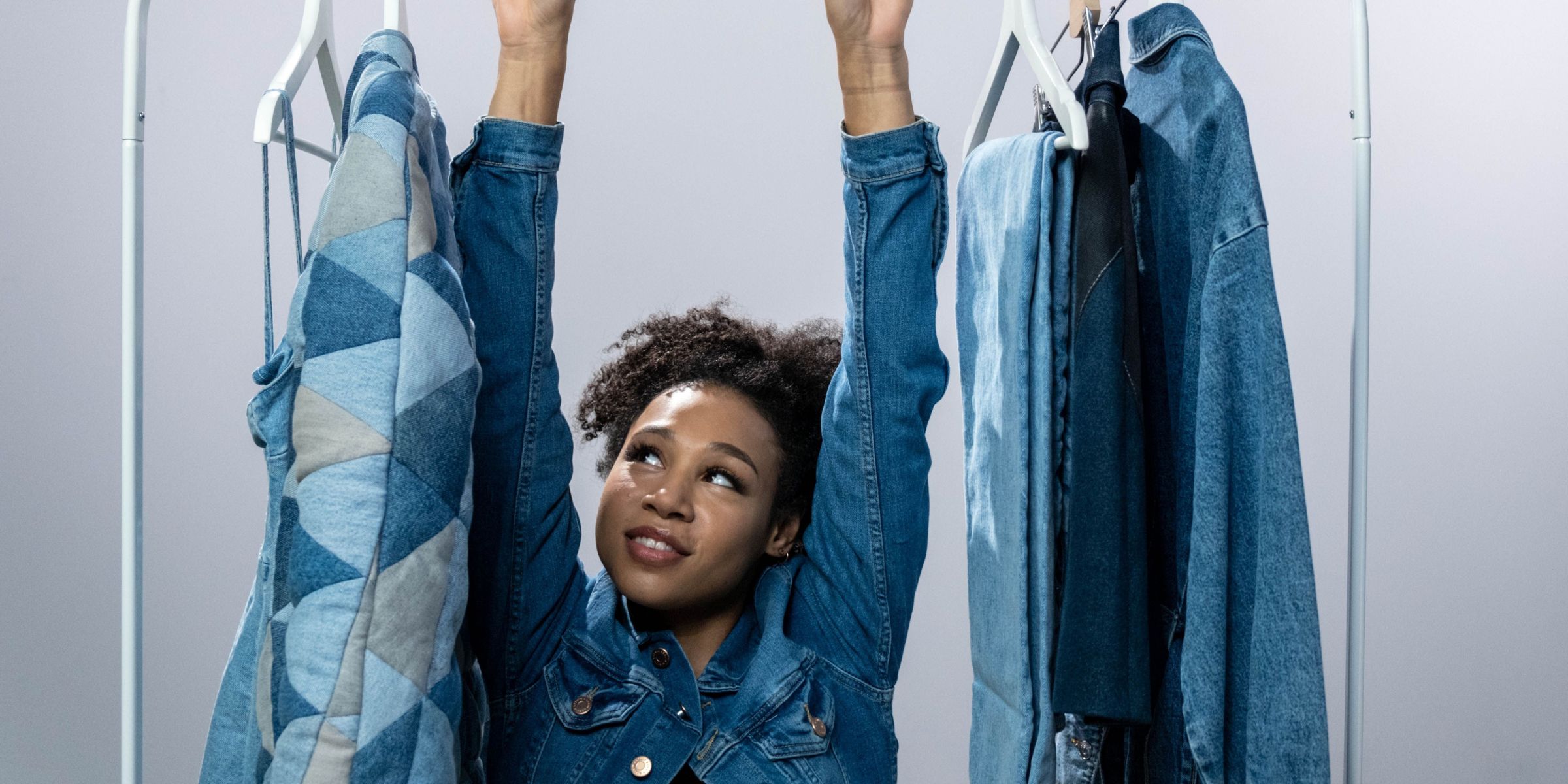A woman wearing a denim jacket and standing in the middle of a clothes rack with assorted denim clothing | Source: Pexels