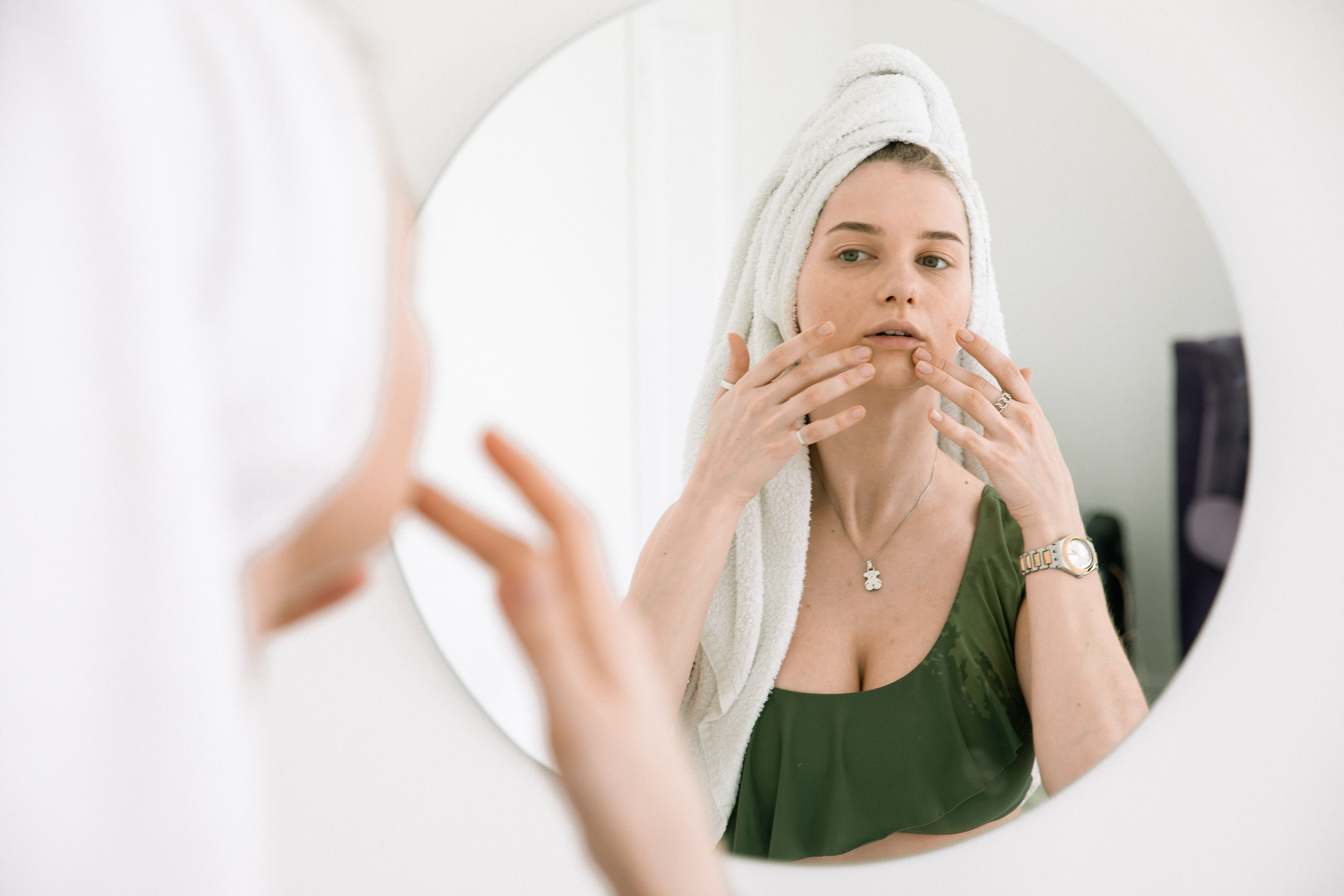 A woman with a towel wrapped around her head studying her face in the mirror | Source: Pexels