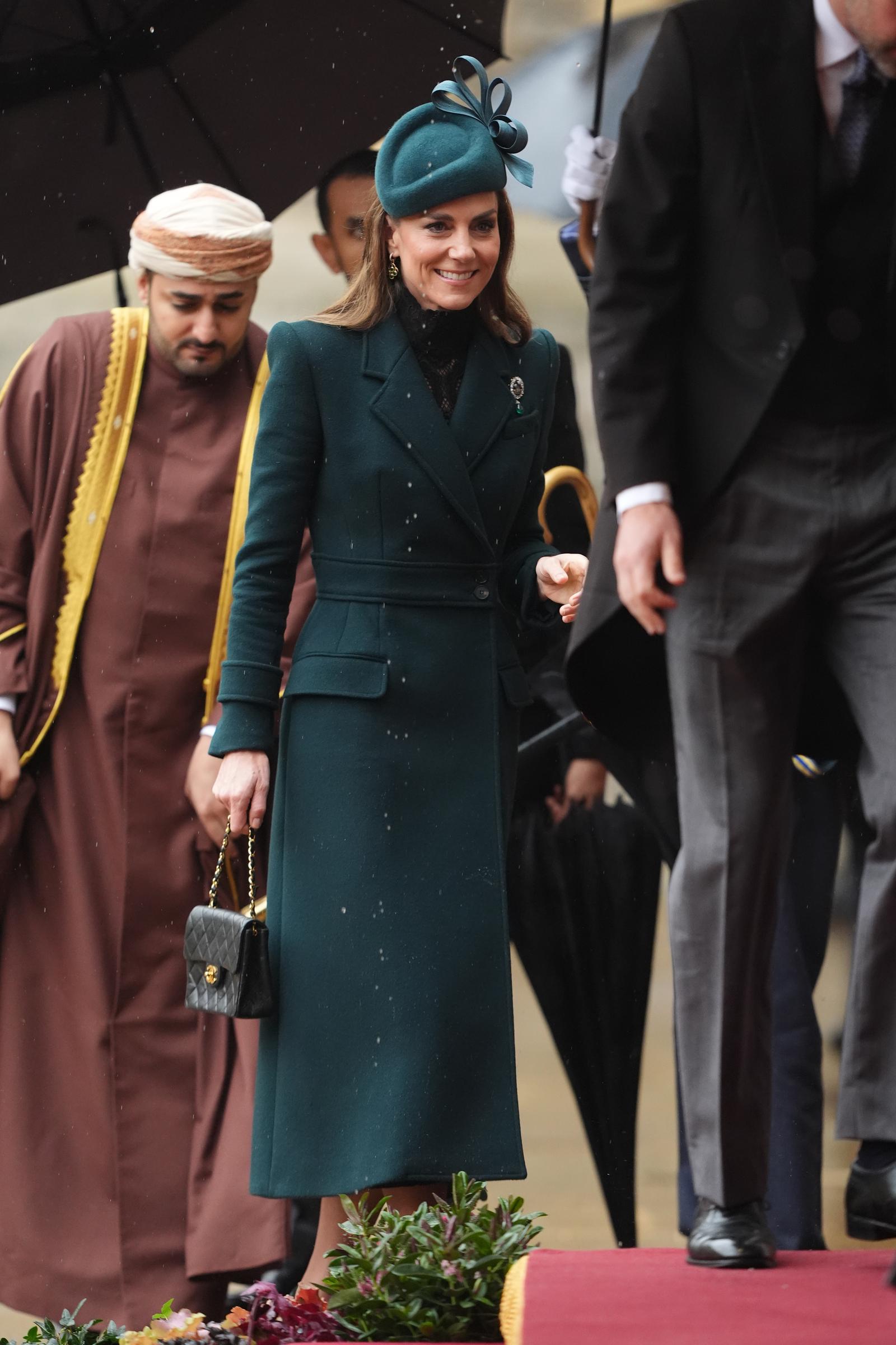 Catherine, Princess of Wales, smiles gently as she navigates the damp ceremonial grounds in Windsor on October 20, 2026. Dressed in her structured forest-green coatdress accented by a delicate high-neck black lace underlay and the historic Queen Alexandra Three Feathers Brooch on her lapel, she carries a small black quilted Chanel flap bag while walking near Prince William. | Source: Getty Images