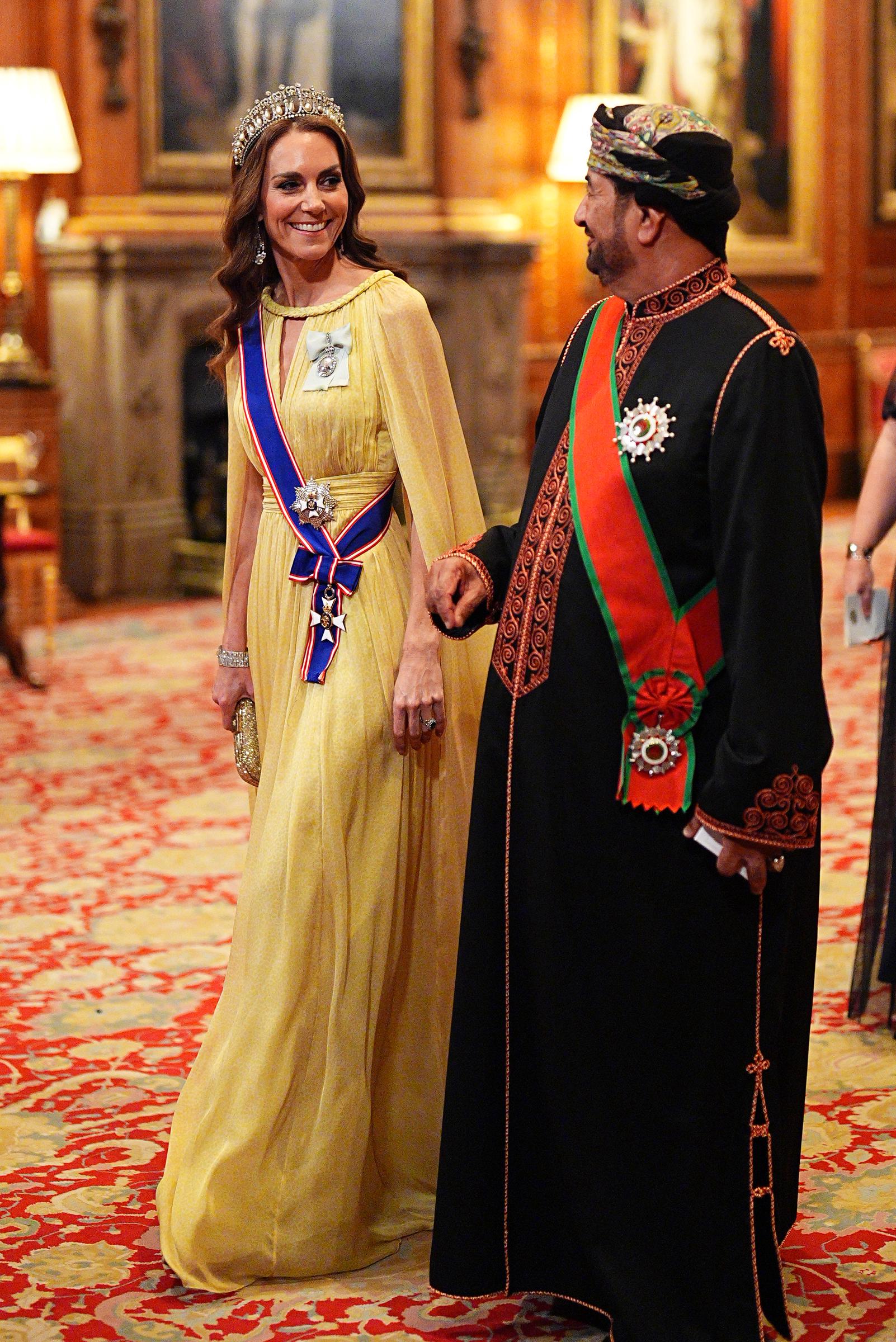 Catherine, Princess of Wales, smiles and converses with H.E. Sayyid Khalid Hilal Al Busaidy as they walk in procession to the state banquet inside Windsor Castle on October 20, 2026. The Princess of Wales stands out in her ethereal yellow Elie Saab cape gown with a braided neckline and Queen Mary's Lover's Knot Tiara, accompanied by the Omani official, who wears a traditional gold-and-red-embroidered bisht, ceremonial sash, and colorful massar turban. | Source: Getty Images