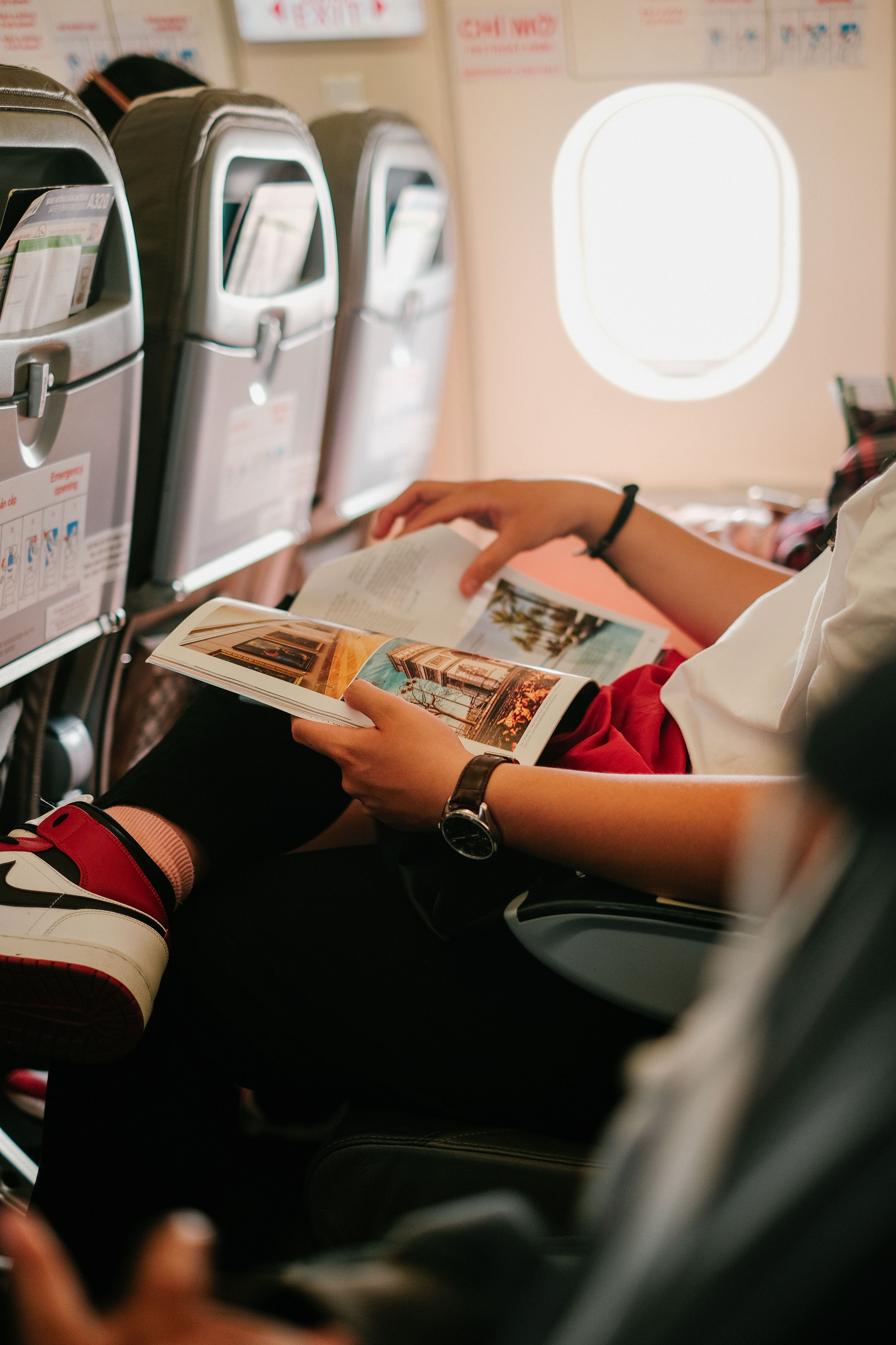Person reading a magazine while seated in a plane's economy section | Source: Pexels