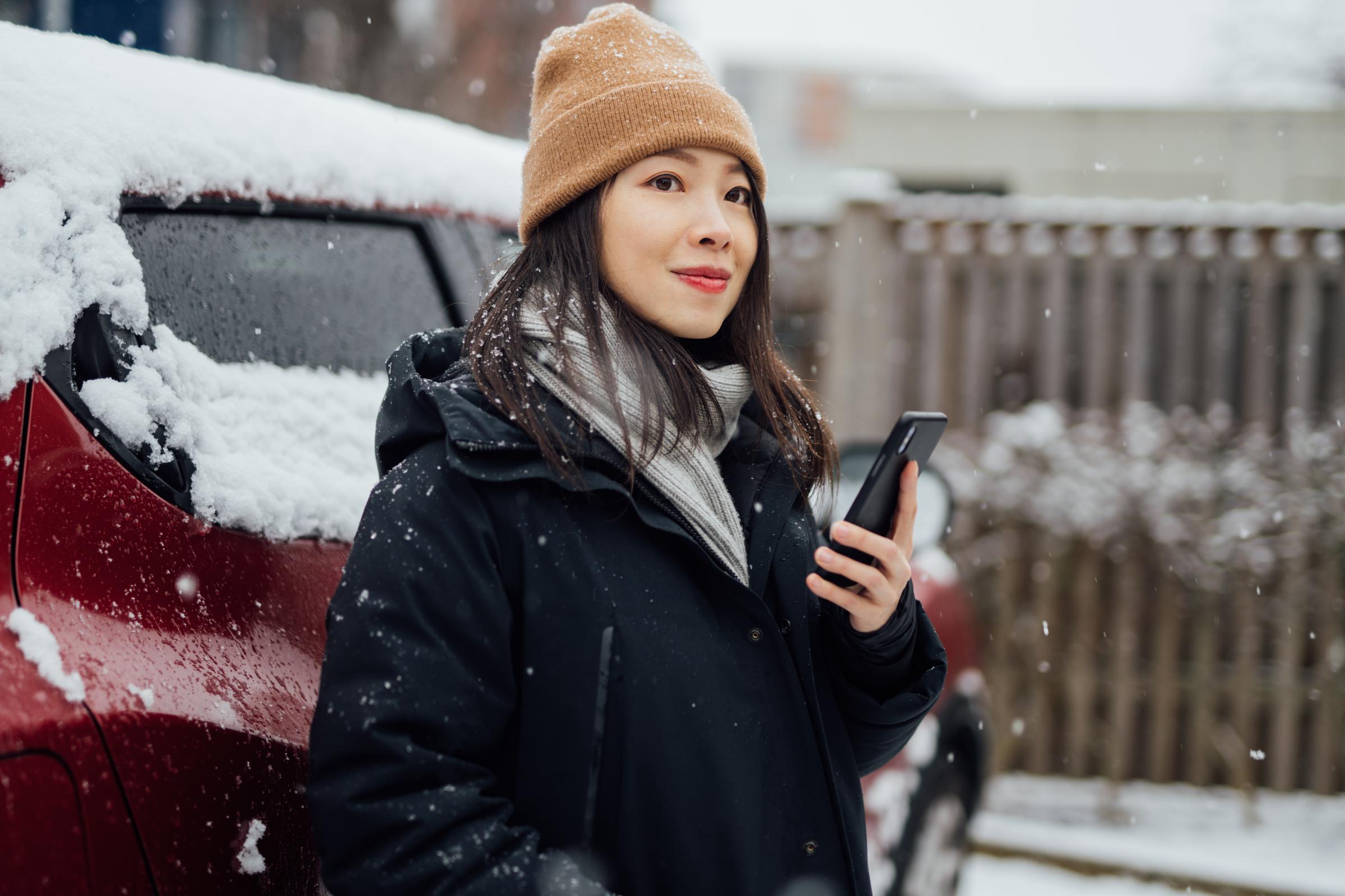 A woman on her phone, standing outside a car in the snow | Source: Getty Images