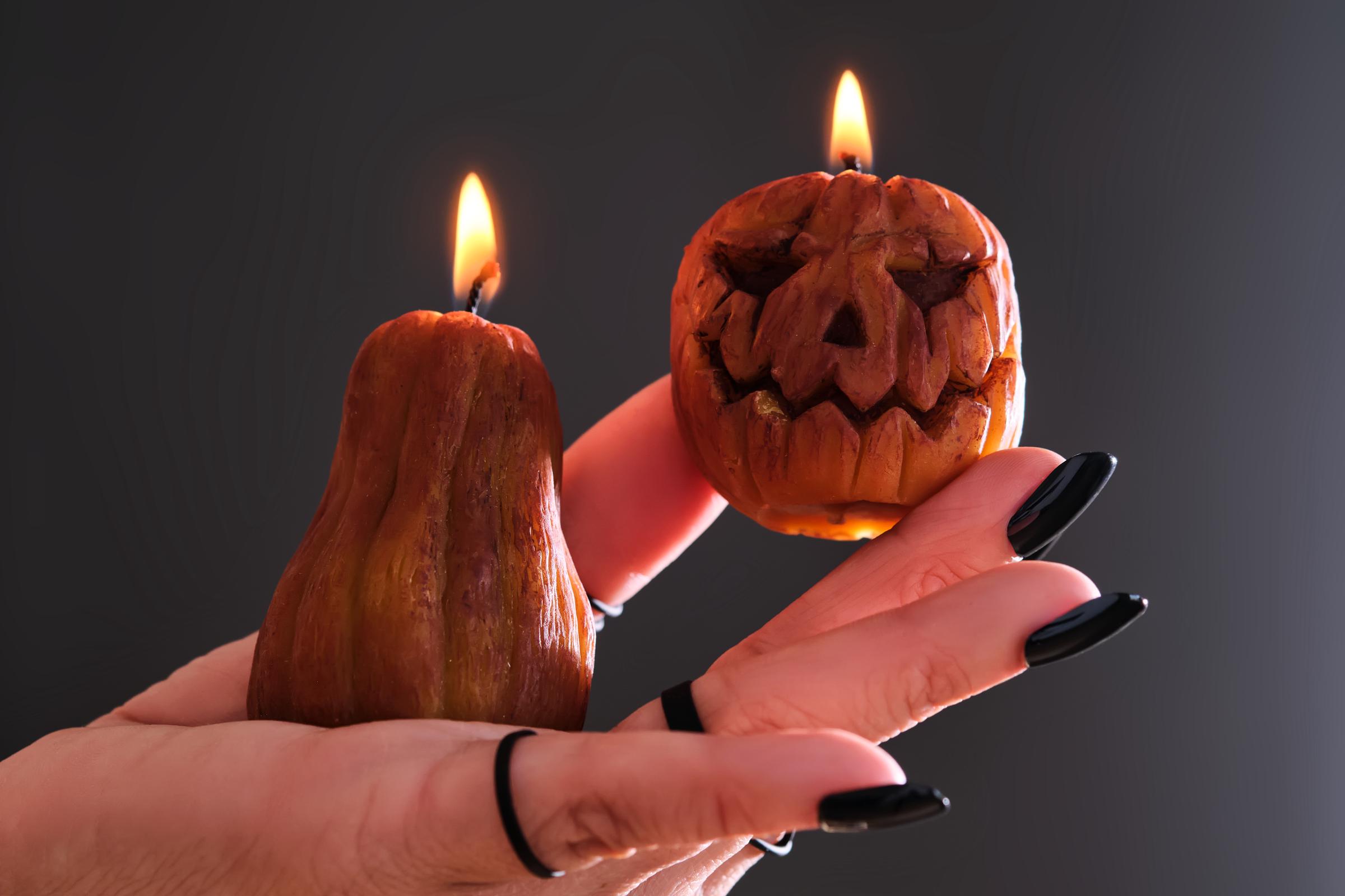 A woman's hand with a black manicure and rings holds two lit candles in the shape of a pumpkin for Halloween | Source: Getty Images