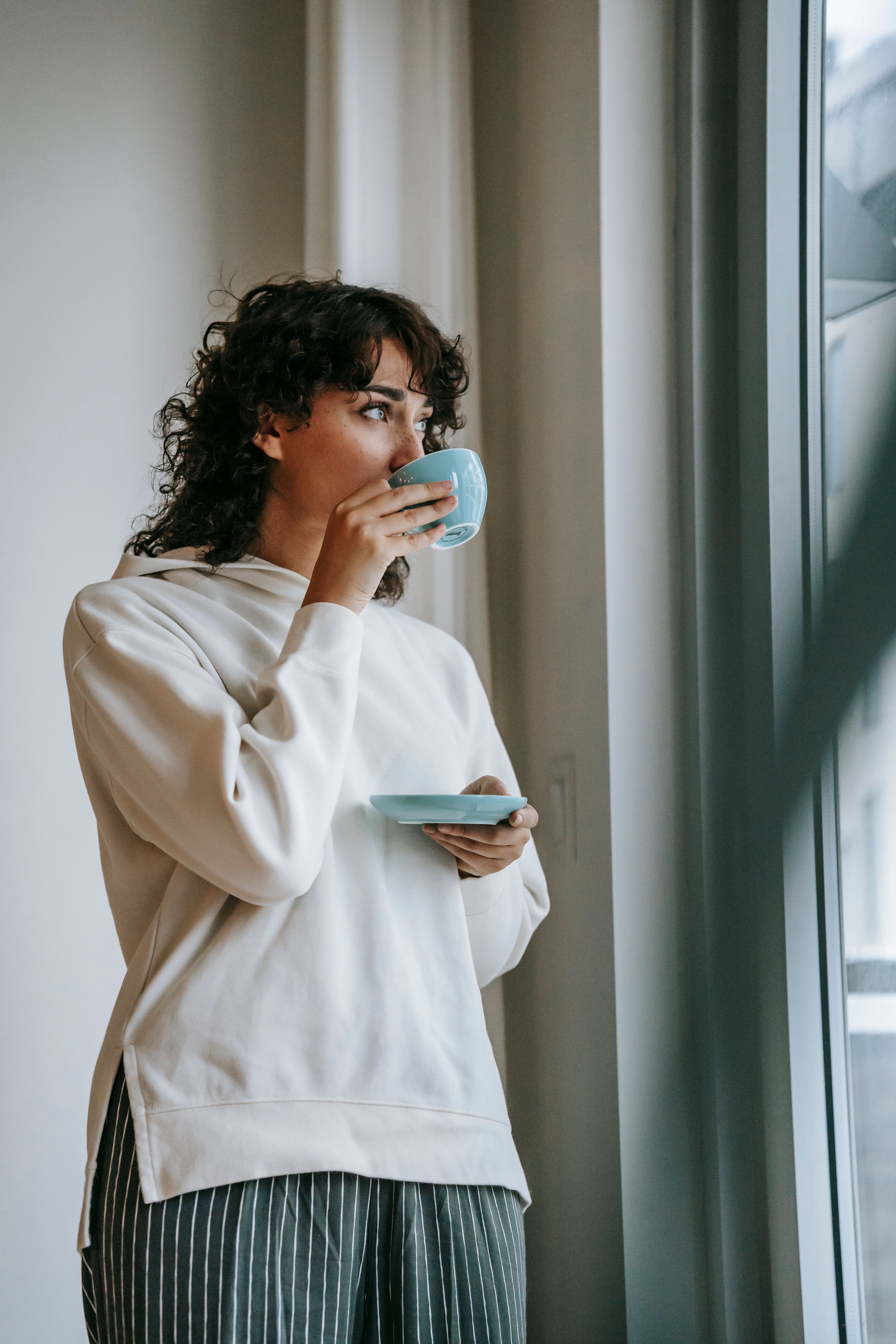A woman drinking coffee while staring out the window | Source: Pexels