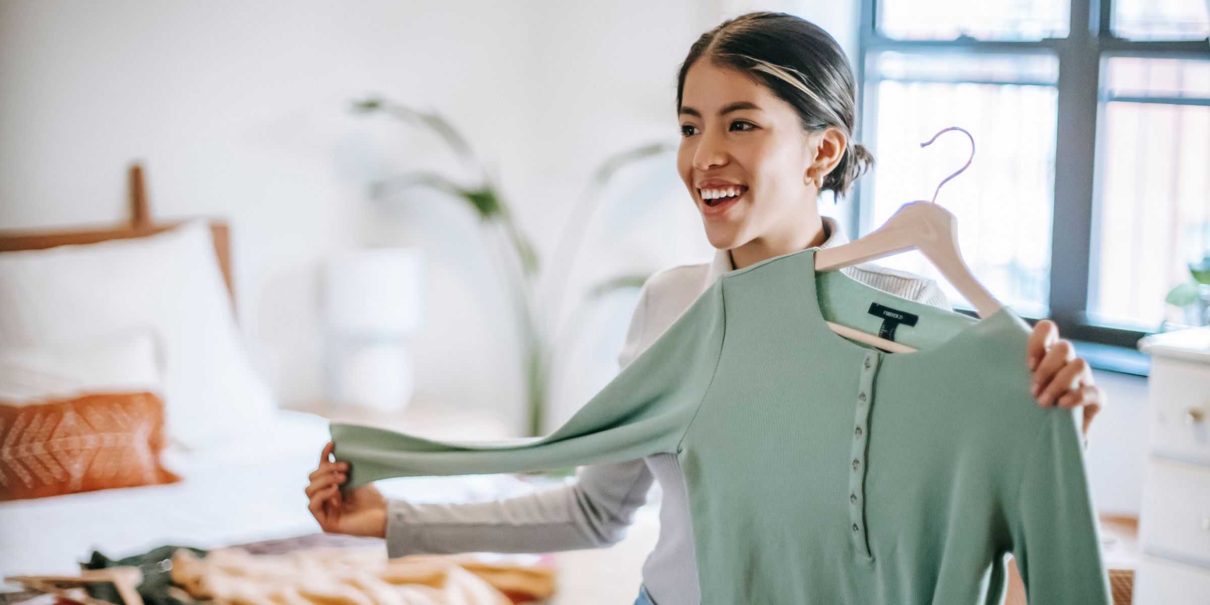 A woman holding up a cardigan in a hanger in a bedroom | Source: Pexels