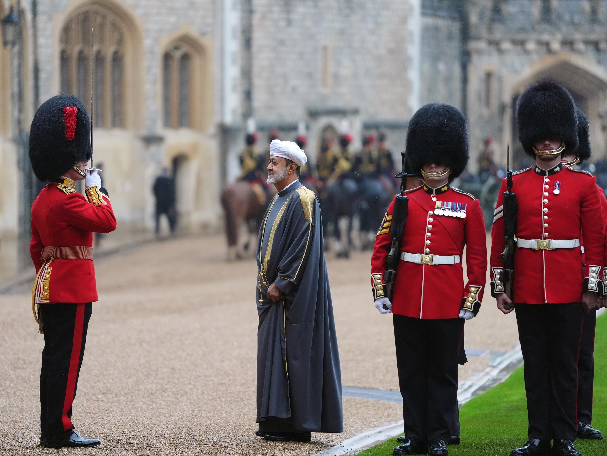 Sultan Haitham bin Tarik of Oman reviews the Guard of Honour during the ceremonial welcome in the Quadrangle of Windsor Castle in Windsor, England, on October 20, 2026. Dressed in an ankle-length grey bisht with gold-embroidered shoulders and trim over a white turban, the visiting monarch stands attentively as an officer in a scarlet tunic and bearskin cap salutes with a raised sword alongside Guardsmen in full ceremonial dress. | Source: Getty Images