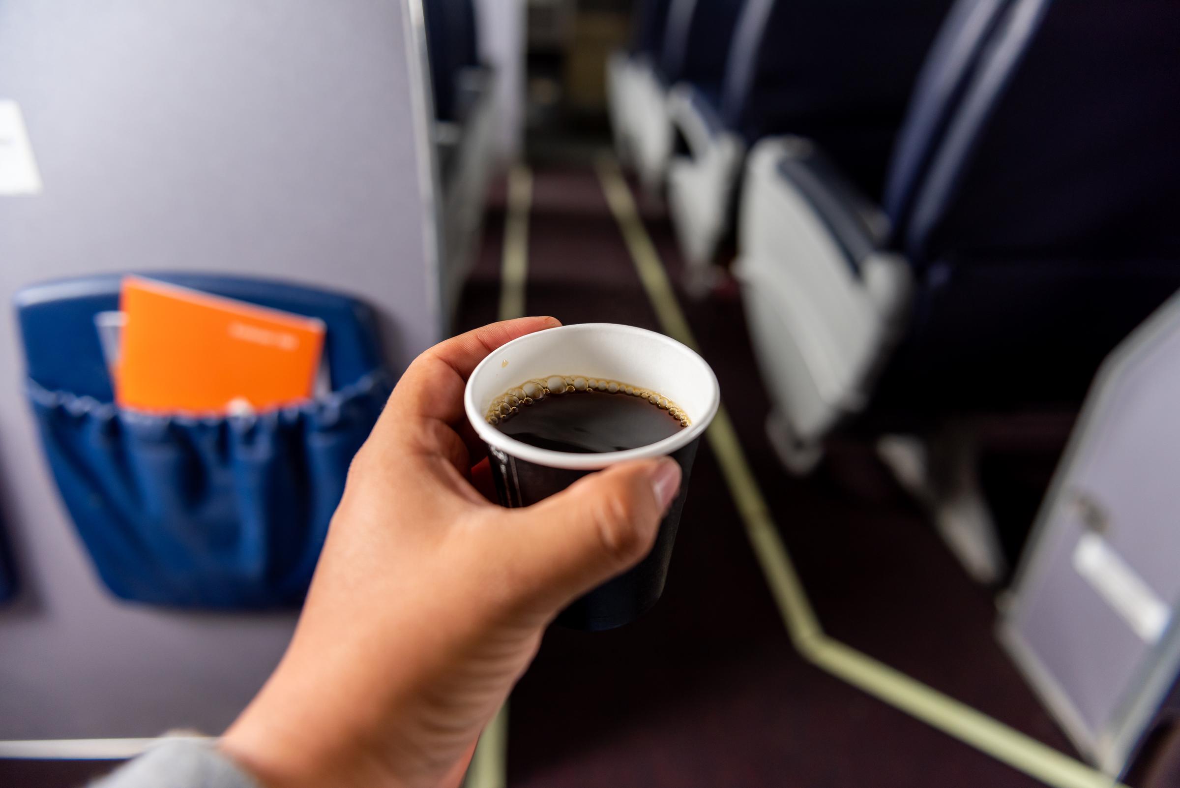 A hand holding a cup of coffee in a plane | Source: Getty Images