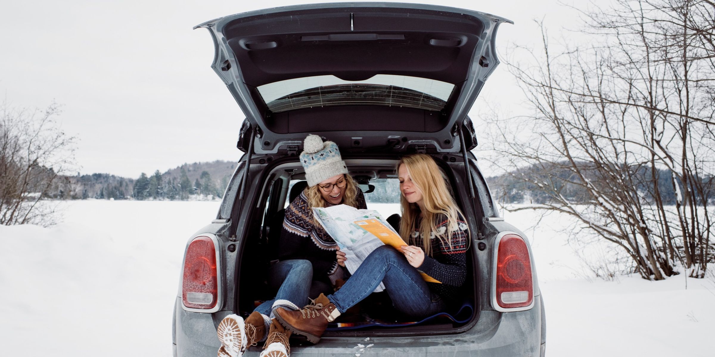 Two women sitting in the truck of a car while reading a map | Source: Getty Images