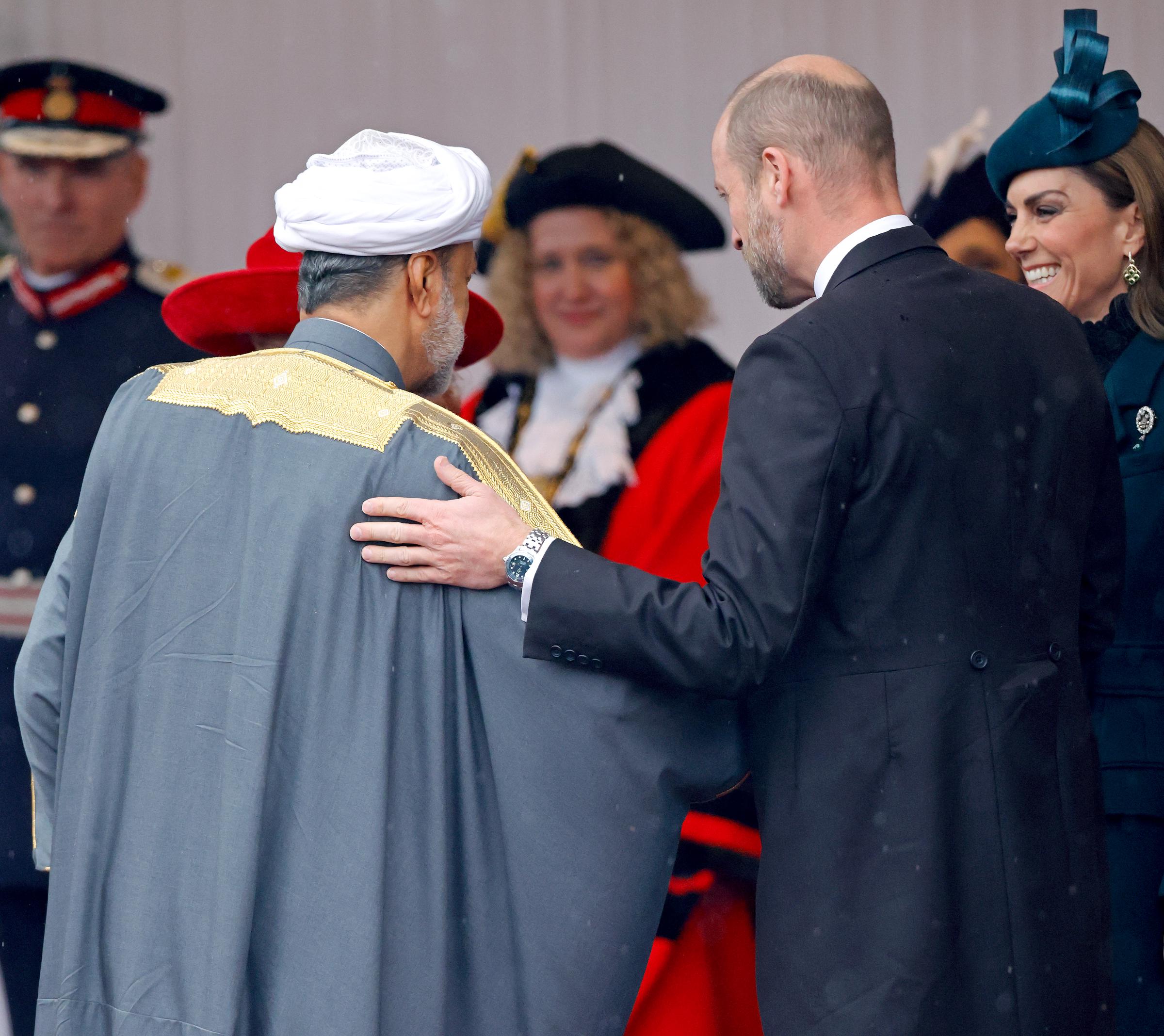 Prince William warmly greets Sultan Haitham bin Tarik of Oman at the Royal Dais on Datchet Road in Windsor, England, on October 20, 2026, marking the start of the three-day state visit. Seen in profile wearing a formal dark morning coat, the Prince of Wales places an affectionate hand on the Sultan's shoulder, as Catherine, Princess of Wales, smiles warmly in the background wearing her emerald-green bespoke fascinator by Juliette millinery and high-neck lace ensemble. | Source: Getty Images