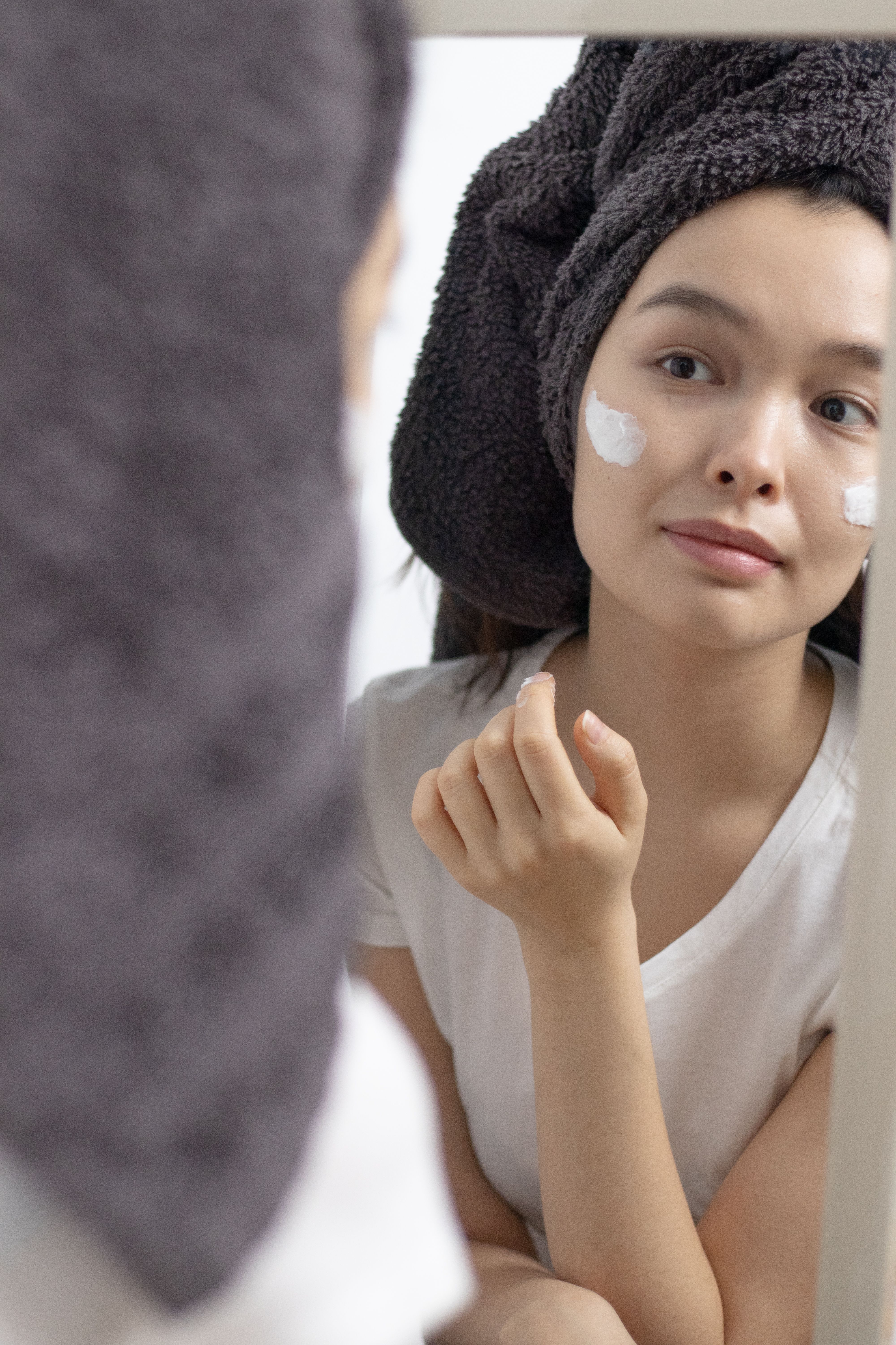 A woman looking in the mirror as she applies moisturizer | Source: Pexels