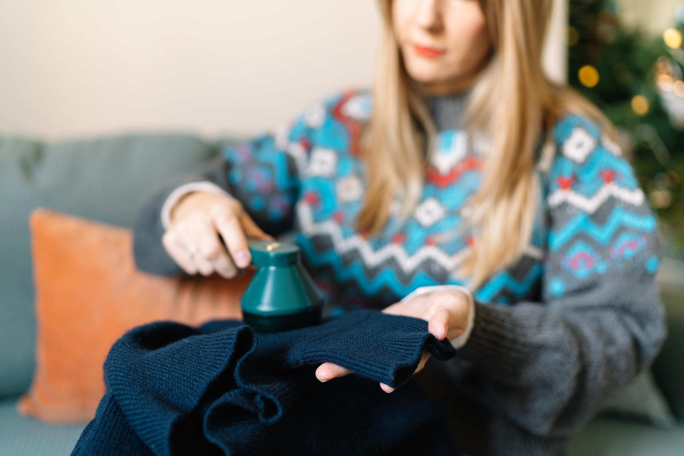 A woman using a fabric shaver to remove lint from her navy sweater | Source: Getty Images