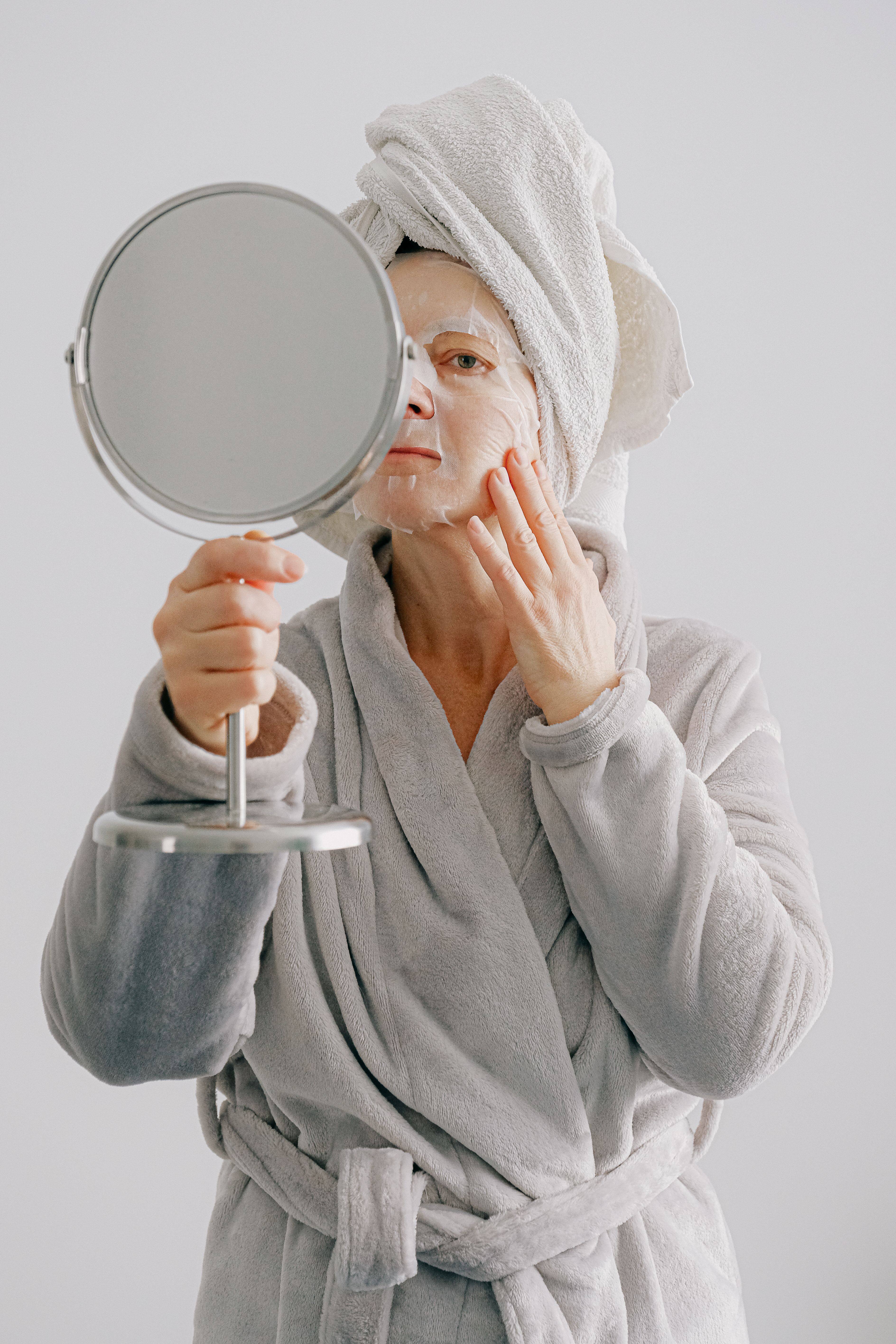 A woman holding up a mirror as she applies a face mask | Source: Pexels