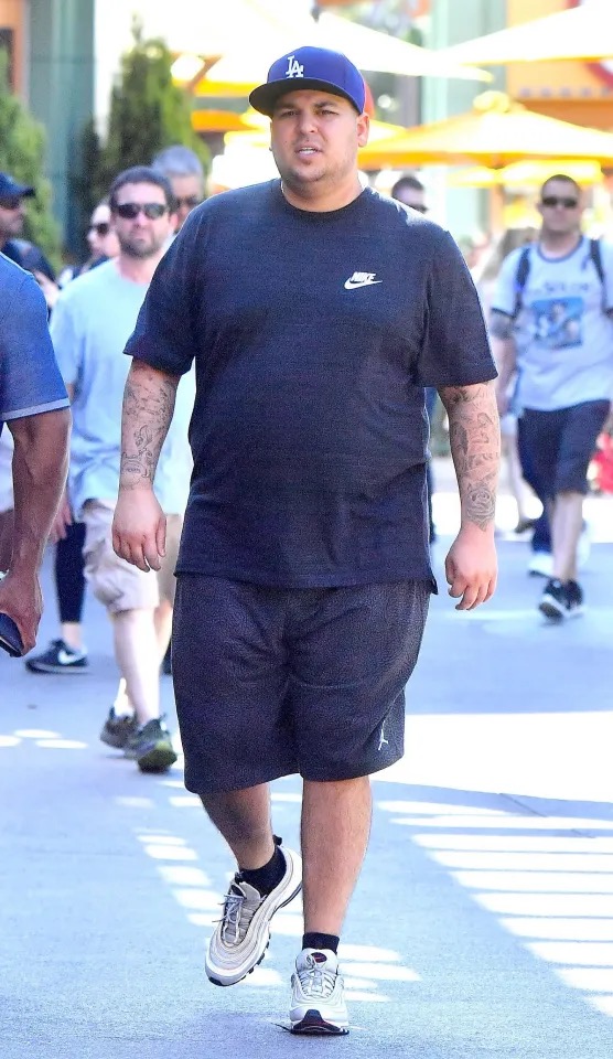 Rob Kardashian is photographed walking outdoors in a black Nike T-shirt, shorts, and an LA baseball cap. The image shows his fuller figure during a period when he was increasingly open about his struggles with weight and body confidence. | Source: The Mega Agency.