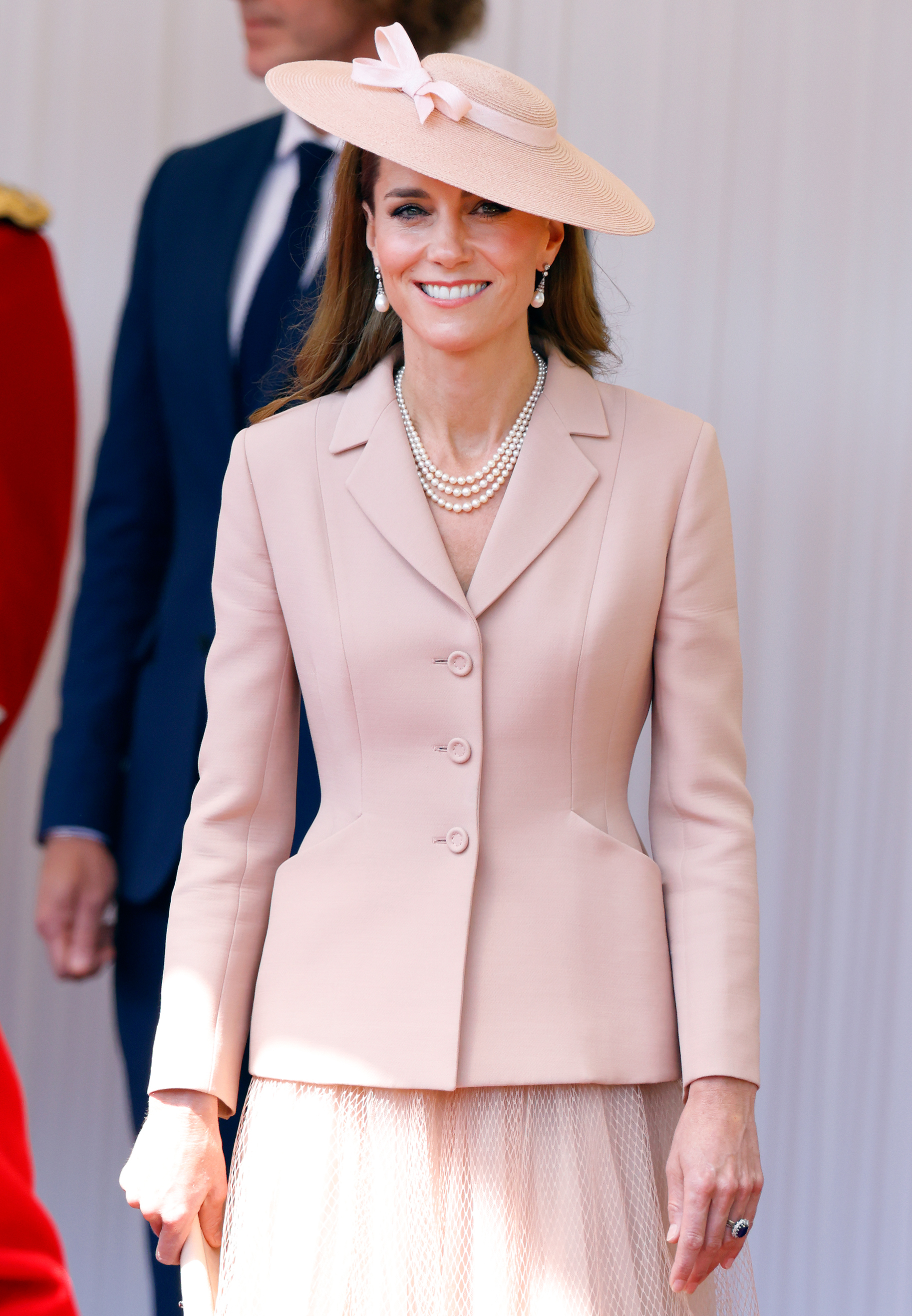 Catherine, Princess of Wales, smiles warmly at the Royal Dais on Datchet Road in Windsor, England, during the formal ceremonial welcome for French President Emmanuel Macron and Brigitte Macron on July 8, 2025. In a nod to French couture diplomacy, Catherine wears a pale blush-pink Christian Dior tailored bar jacket over a matching pleated tulle skirt, beautifully accessorized with Queen Elizabeth II's three-strand pearl necklace, pearl drop earrings, and a tilted saucer hat adorned with a delicate ribbon bow. | Source: Getty Images