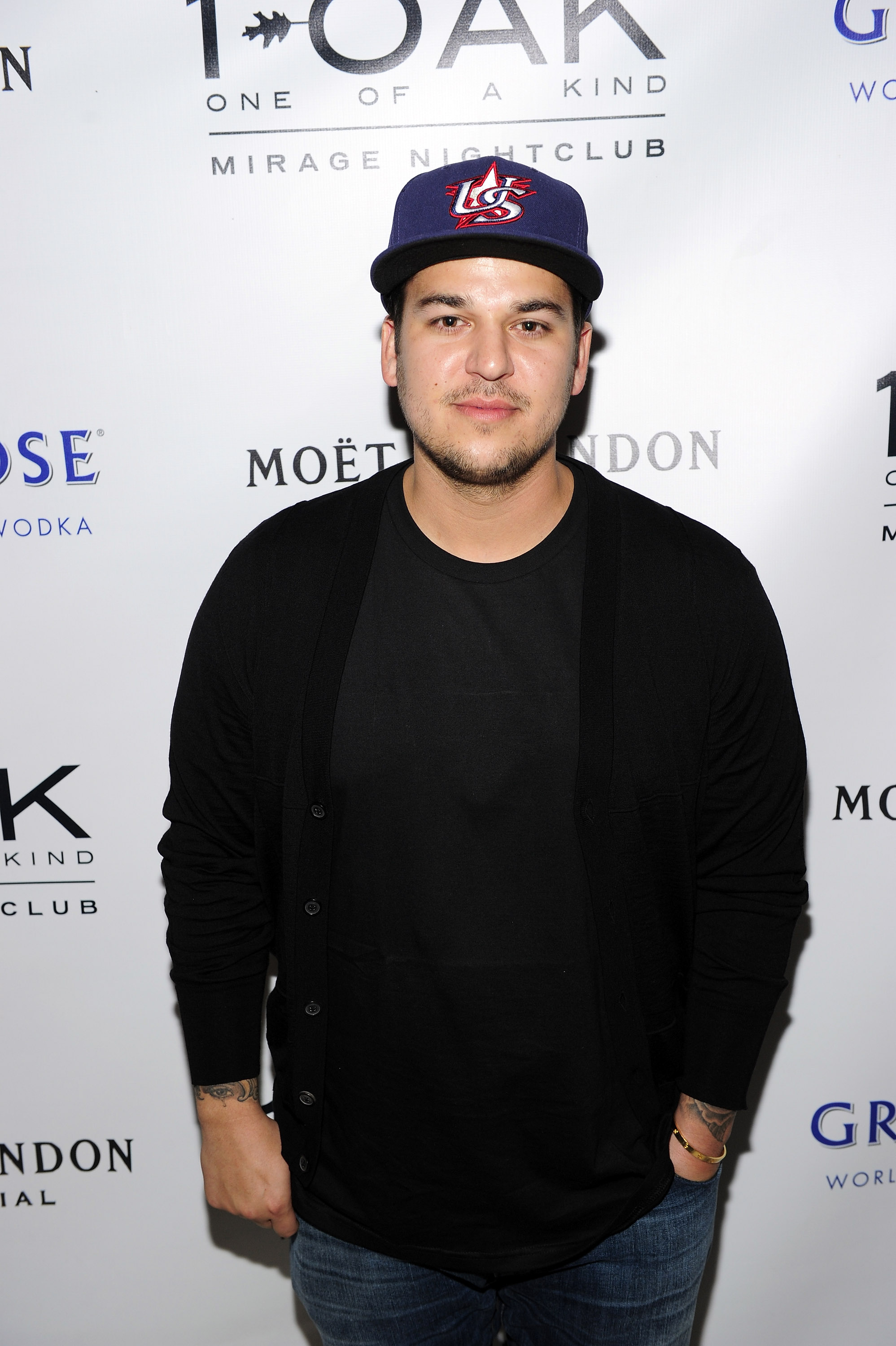 Rob Kardashian poses in a black T-shirt, cardigan, and baseball cap at 1 OAK Nightclub in Las Vegas in May 2013. His appearance came during a period when his changing weight was becoming a subject of public scrutiny, affecting his confidence and willingness to attend events. | Source: Getty Images.