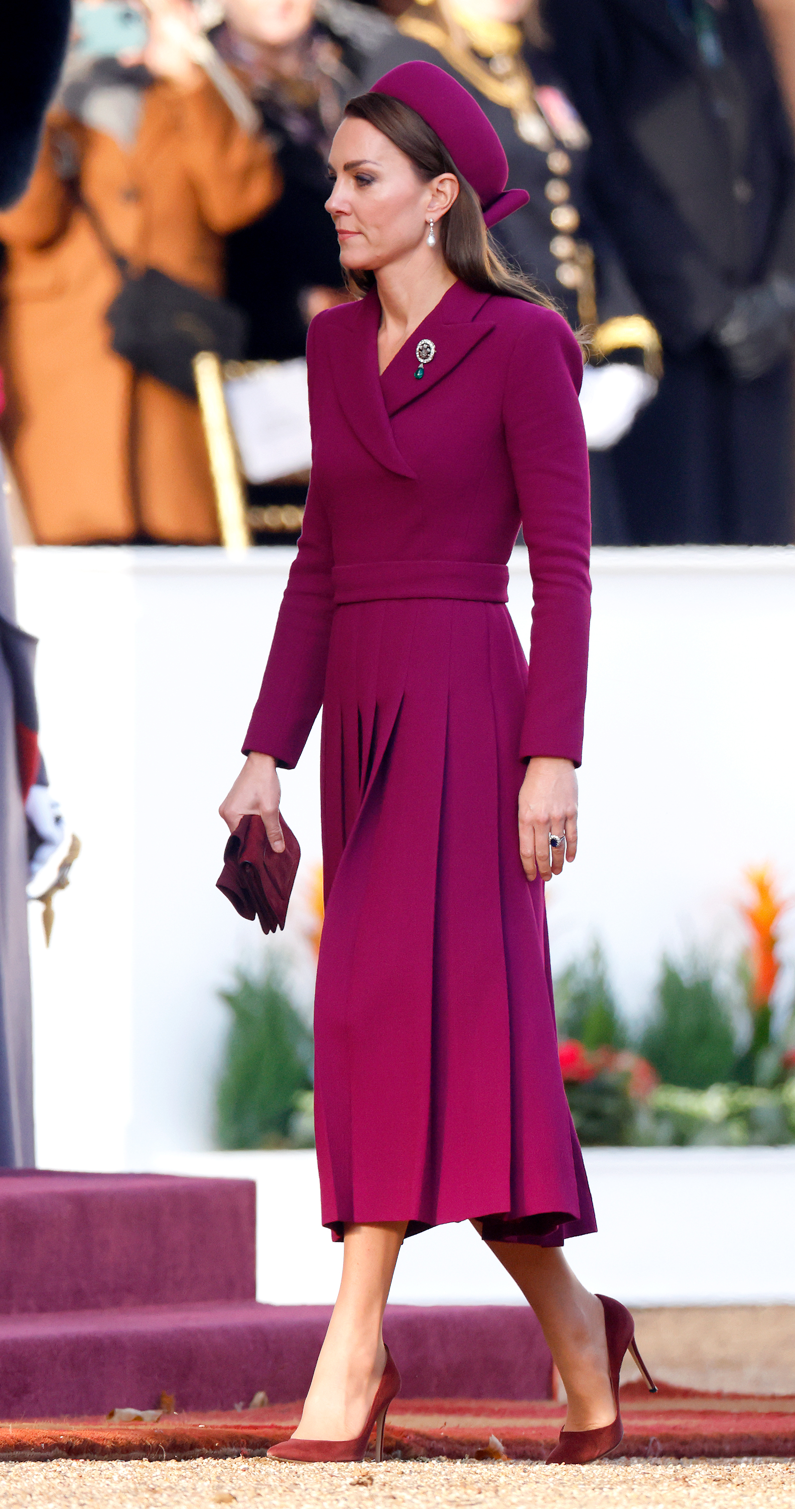 Catherine, Princess of Wales, arrives at Horse Guards Parade in London on November 22, 2022, for the ceremonial welcome of South African President Cyril Ramaphosa during the first state visit hosted under King Charles III's reign. Stepping out in head-to-toe magenta, she wears a tailored Emilia Wickstead coatdress with an asymmetrical collar, belted waist, and pleated skirt, styled with a coordinating Sean Barrett pillbox hat, burgundy suede pumps and gloves, Princess Diana's pearl drop earrings, and the Queen Alexandra Three Feathers Brooch pinned to her lapel. | Source: Getty Images