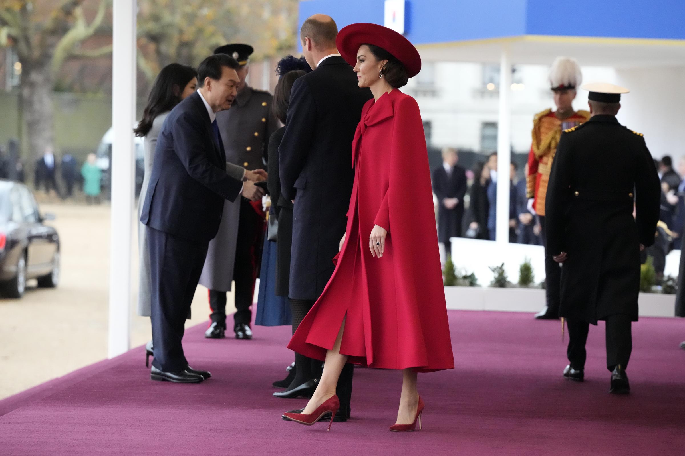Catherine, Princess of Wales, makes a dramatic entrance onto the dais at Horse Guards Parade in London on November 21, 2023, during the ceremonial welcome for the South Korean State Visit. The royal commands the pavilion in a monochrome scarlet ensemble, wearing a bespoke Catherine Walker cape coat with an oversized bow over a matching red dress, complete with a wide-brimmed Sarah Cant hat, Princess Diana's sapphire and diamond drop earrings, and red suede Gianvito Rossi pumps. | Source: Getty Images