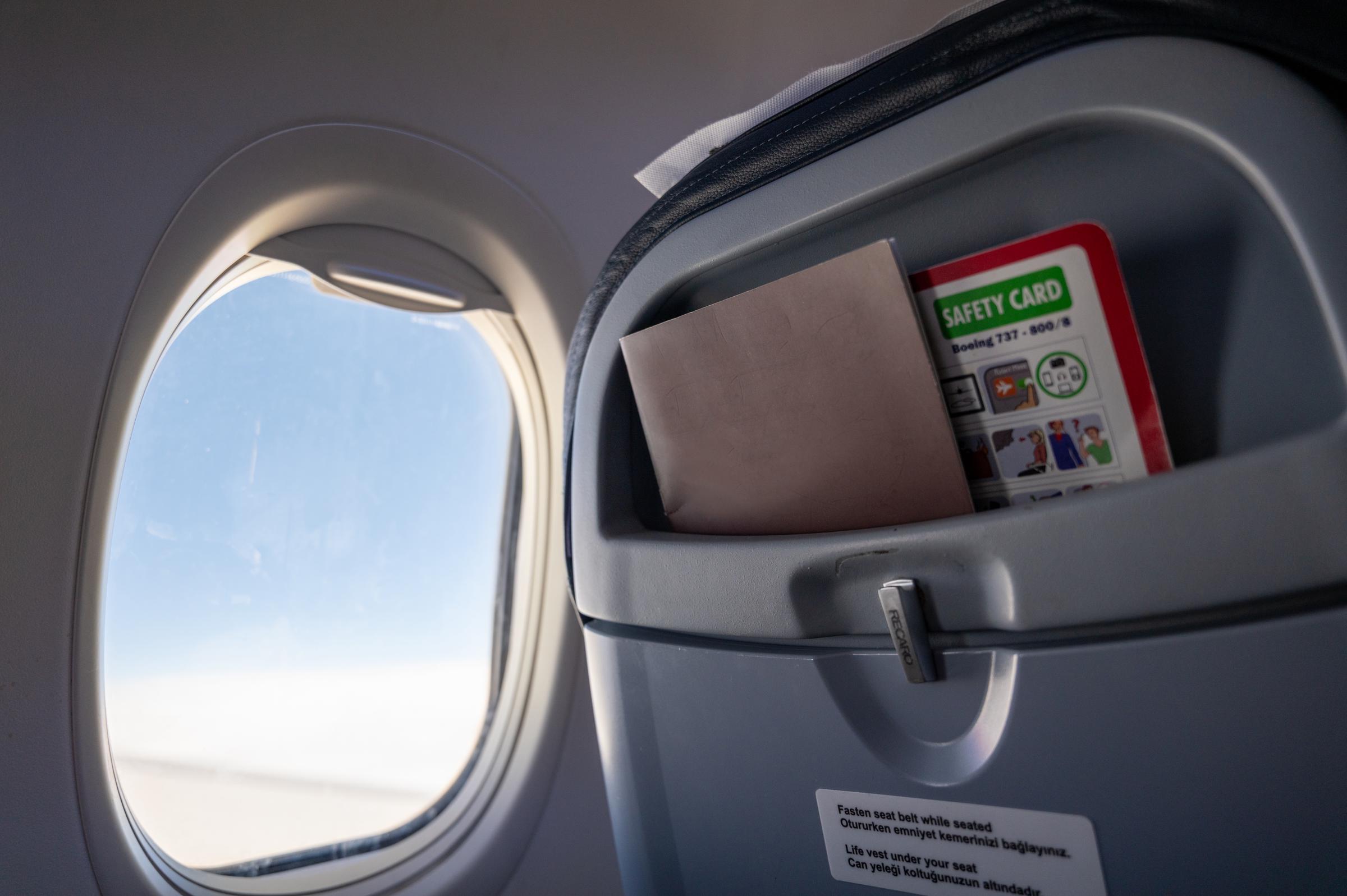 An airplane safety card and magazine tucked into the seat pocket during a flight | Source: Getty Images