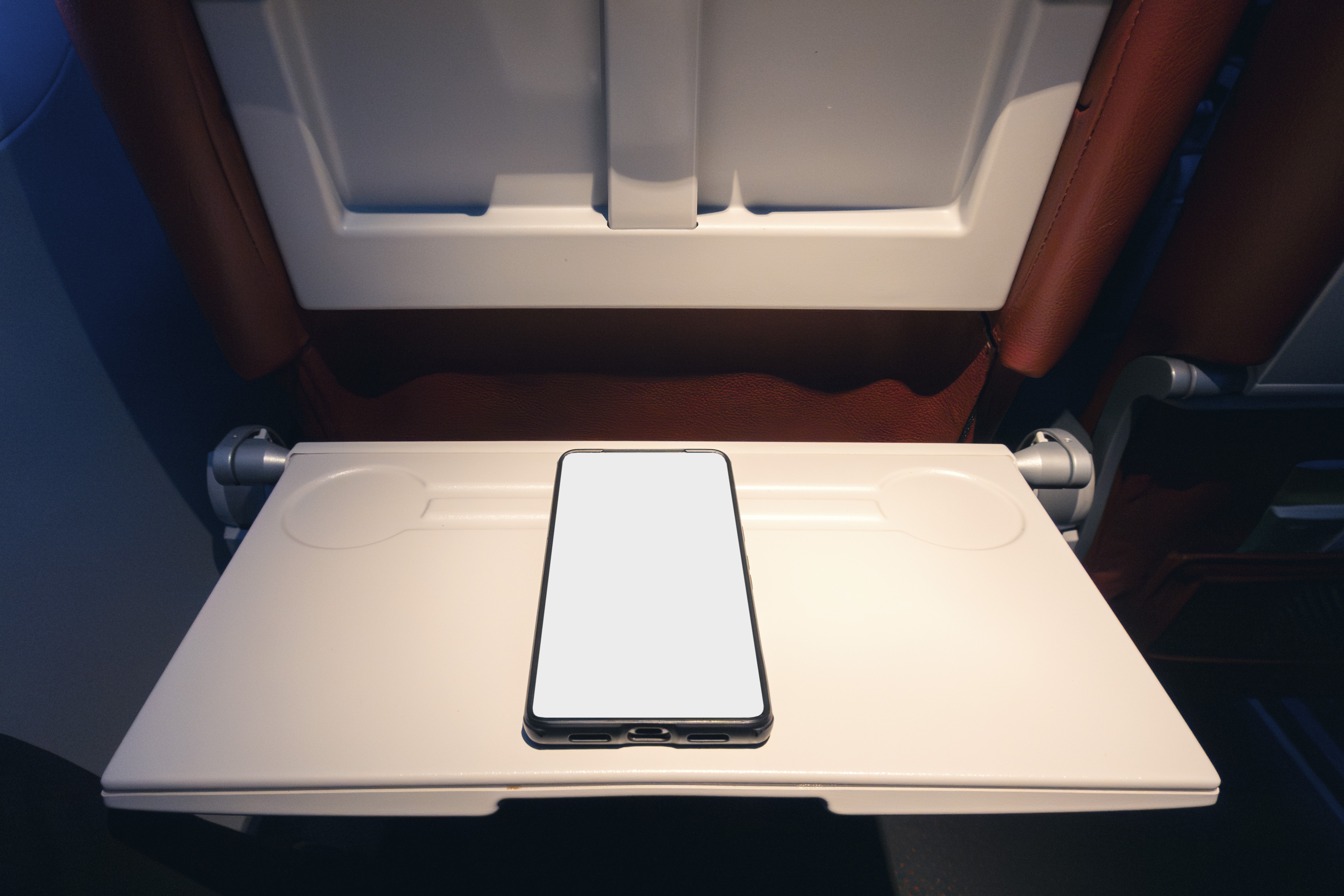 A smartphone lies on a closed tray table in an airplane | Source: Getty Images