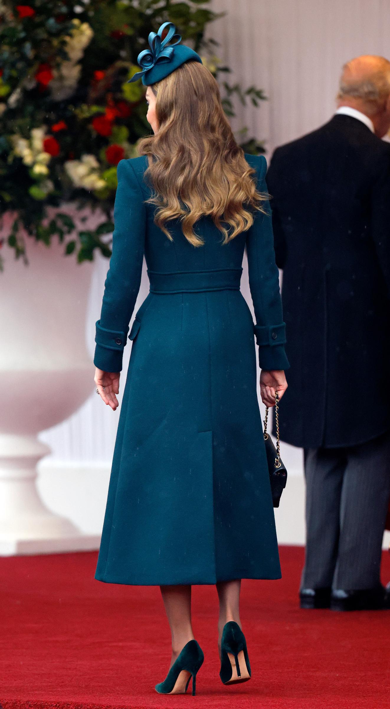 A rear view of Catherine, Princess of Wales, highlights the clean lines of her tailored midi coatdress as she walks across the red carpet in Windsor on October 20, 2026. The back of the deep green ensemble reveals a defined waist belt and a center kick pleat, complemented by soft brunette waves flowing beneath a Juliette millinery fascinator, velvet stiletto pumps, and a quilted Chanel handbag held by its chain strap. | Source: Getty Images