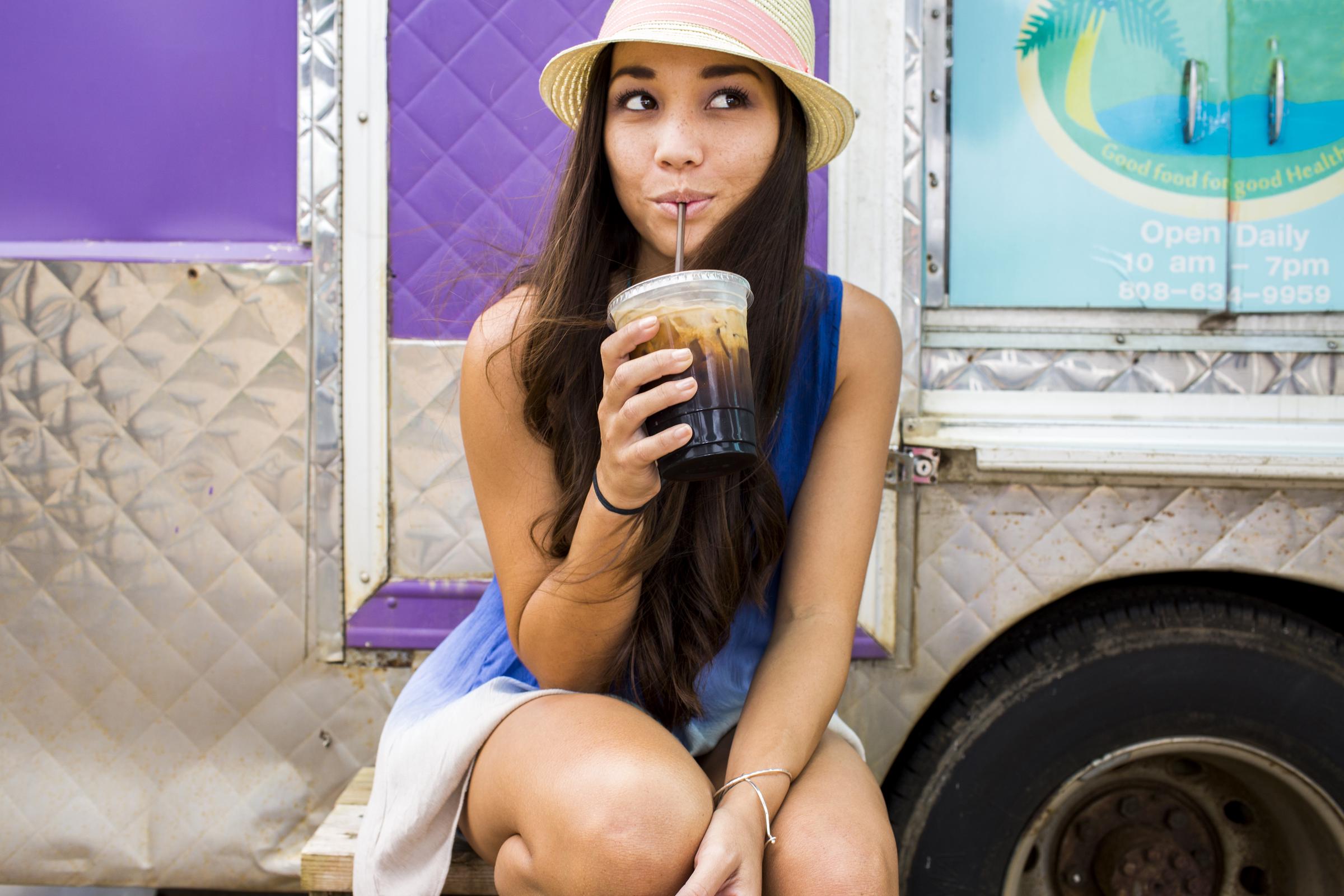 A woman drinking iced coffee near a food cart | Source: Getty Images