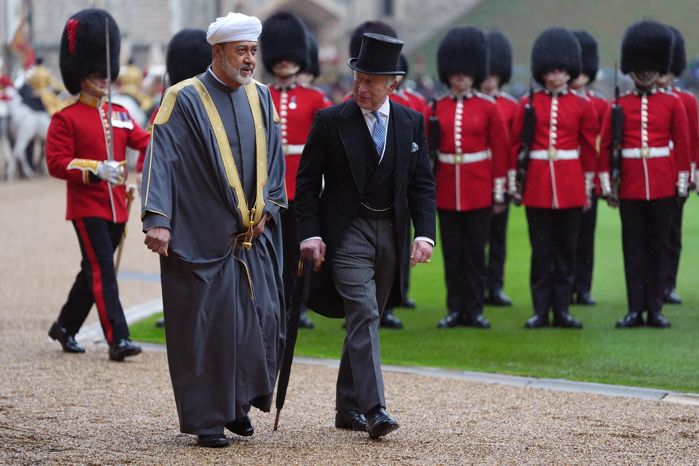 King Charles III and Sultan Haitham bin Tarik of Oman inspect the military guard during the formal ceremonial welcome at Windsor Castle in Windsor, England, on October 20, 2026. As Guardsmen in scarlet tunics and tall bearskin caps stand in formation behind them, King Charles III looks classic in a black morning coat, pinstriped trousers, and a silk top hat while holding an umbrella, walking alongside the Sultan, who wears a traditional grey bisht accented with gold embroidery and a white turban. | Source: Getty Images